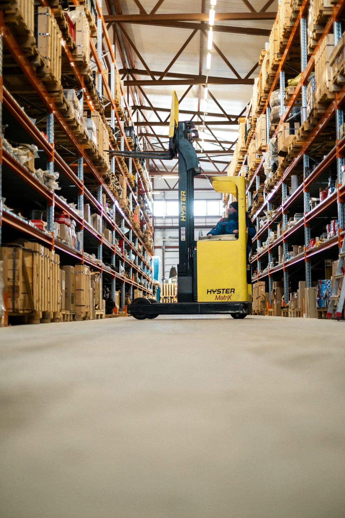 A forklift operator working between tall shelving racks in an industrial warehouse